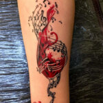 Ein Tattoo in schwarz-rot als Motiv eine Mischung aus Weinglas und Musiknoten