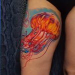 Bein Tattoo einer Feuerqualle in orange auf blauem Grund